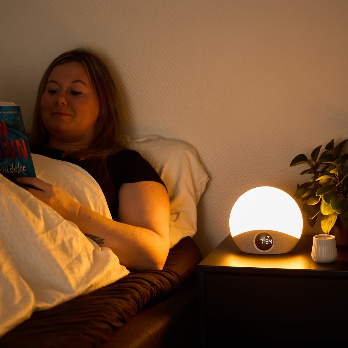 Kvinna läser i sängen med väckarklockan tänd som läslampa på nattduksbordet