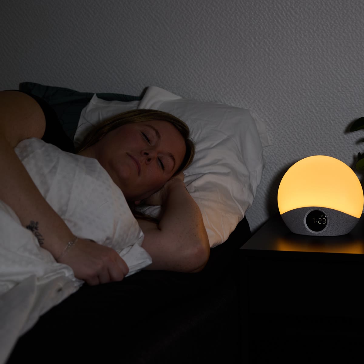 Kvinna sover bredvid väckarklockan som lyser svagt orange